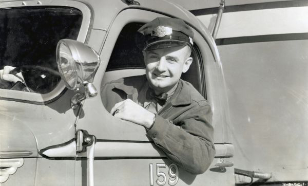 Davis Campbell, Decatur Cartage Company's safe driver, leans out the driver's window of an International truck, smiling.